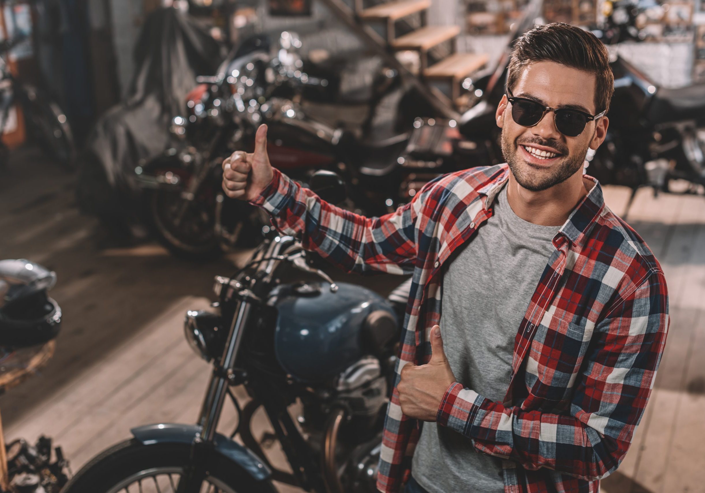 happy handsome motorcyclist with thumbs up in repair shop with classic motorbikes